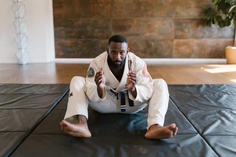Martial artist wearing a gi sits on a mat, ready for training indoors.