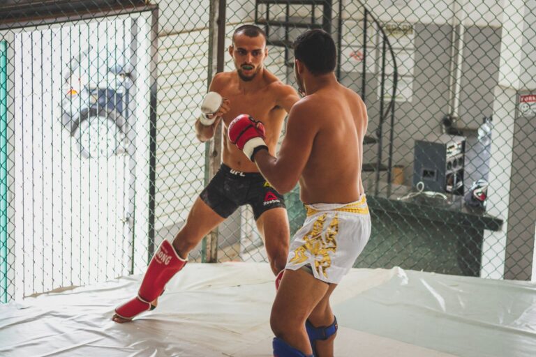 Two men engage in intense kickboxing sparring inside a gym arena.