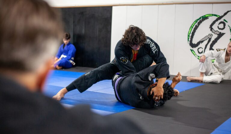 Martial artists in black gi engage in practice on gym mats. Indoor training session.