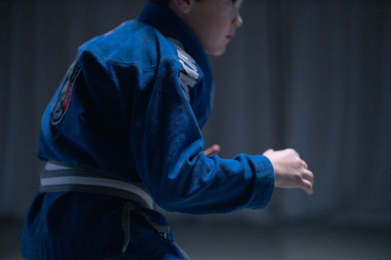 A young boy in a blue gi practicing Brazilian Jiu-Jitsu indoors.