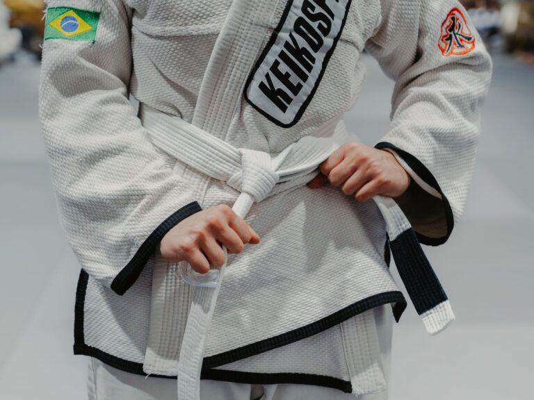 Close-up image of a martial artist tying their judo gi belt, showcasing Brazilian and Keiko logos.