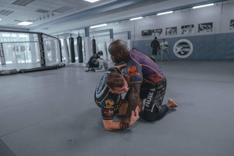 Two men engaged in a focused martial arts training session on a gym mat indoors.