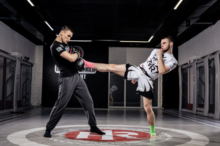 Two men practice kickboxing in a professional gym environment, showcasing dynamic movement and sport.