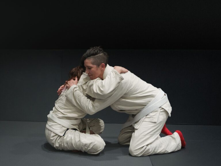 Two adults practicing Brazilian Jiu-Jitsu in a dojo in Buenos Aires.
