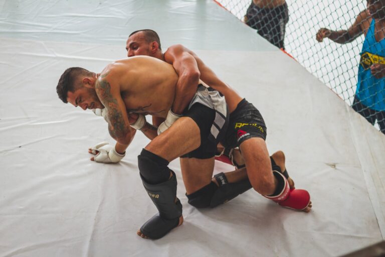 Two male athletes engage in intense grappling during MMA training session indoors.
