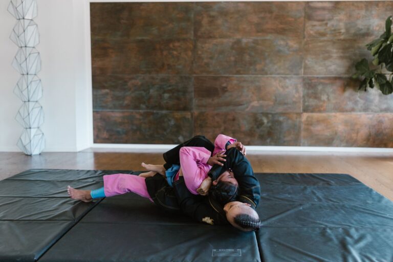 Martial artists in grappling position on mats during training session indoors.