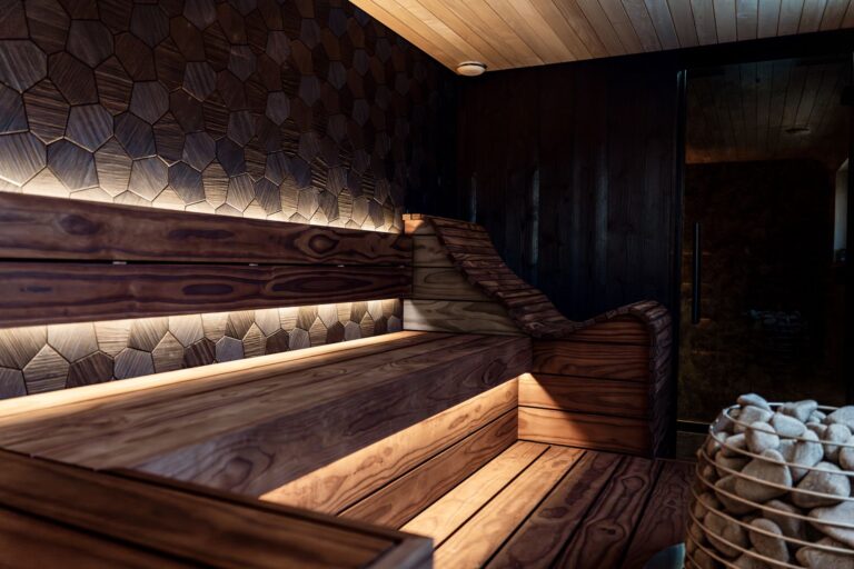 A stylish modern indoor sauna featuring LED lighting, wooden benches, and a unique hexagonal wall design.