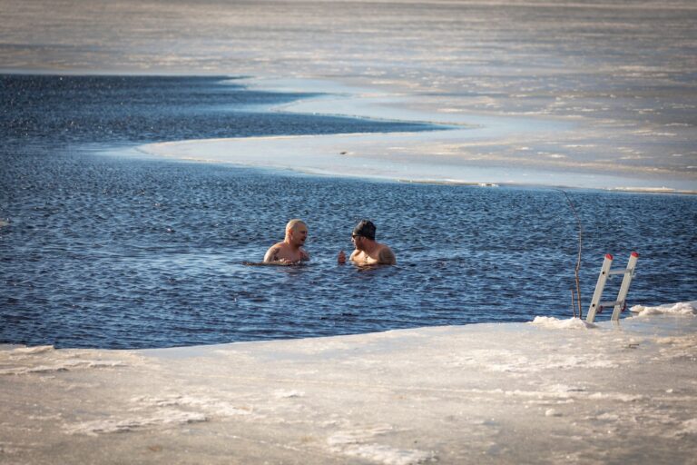 Two men brave the cold for a swim in a partially frozen lake during winter.